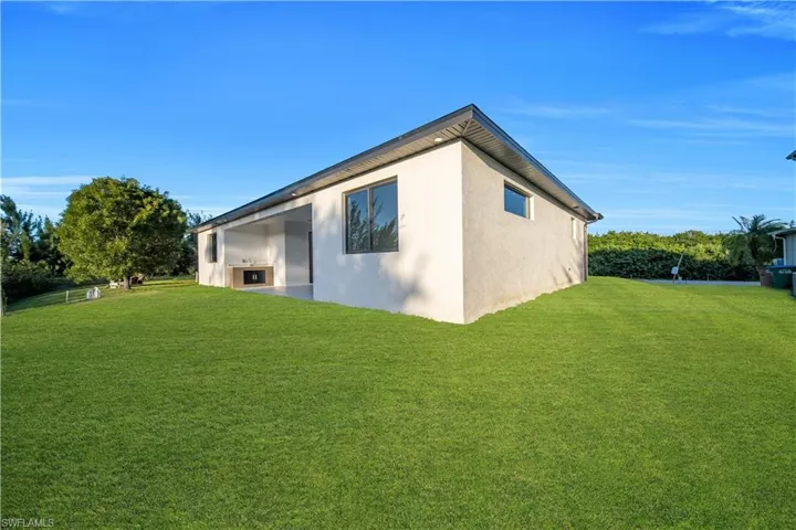 Stucco exterior featuring a covered patio, built-in outdoor kitchen, recessed lighting, and expansive lawn