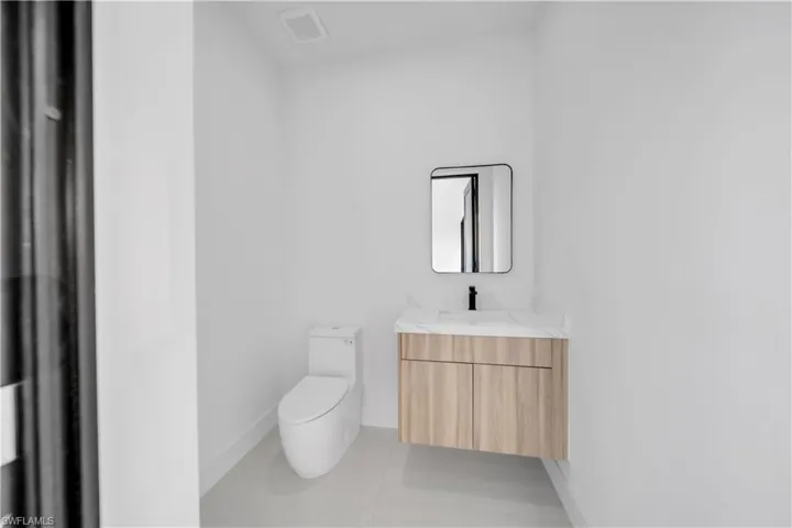 Floating vanity with wood-finish cabinetry, stone-surface countertop, rectangular undermount sink, matte black faucet, and modern square-cornered mirror