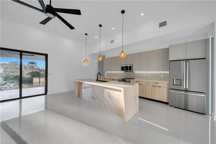 Kitchen featuring a waterfall island with stone-finish surfaces, integrated under-cabinet lighting, high-gloss cabinetry, stainless steel appliances, and large-format tile flooring