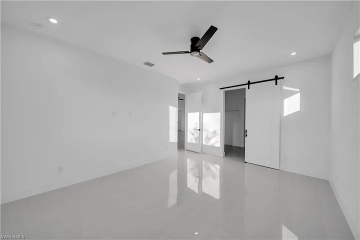Interior space featuring large-format tile flooring, recessed lighting, matte black ceiling fan, and a white sliding barn door with black hardware
