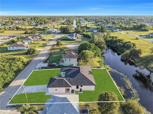 Aerial perspective featuring a single-story residence with a multi-gabled shingle roof, paved driveway, concrete walkway, and canal-front lot