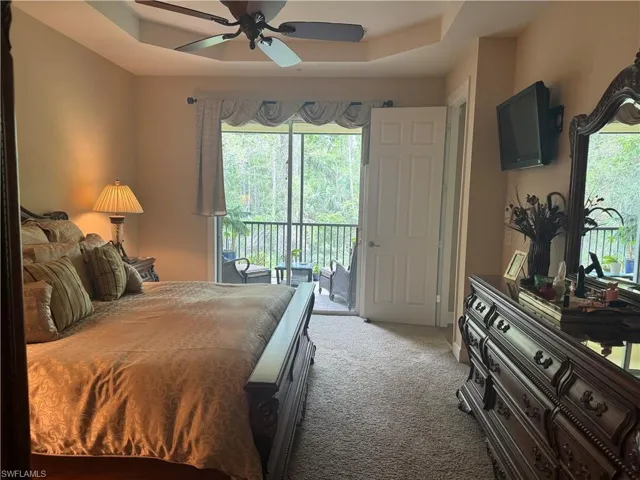Carpeted bedroom with access to exterior, a raised ceiling, and ceiling fan