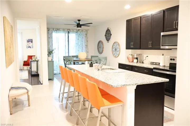 Kitchen with stainless steel appliances, a kitchen bar, a ceiling fan, light stone countertops, and a kitchen island with sink
