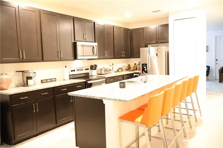Kitchen featuring appliances with stainless steel finishes, a kitchen bar, light stone countertops, and dark brown cabinets