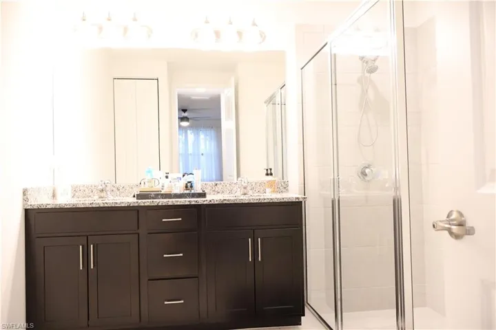 Full bathroom featuring a shower stall, double vanity, and a ceiling fan
