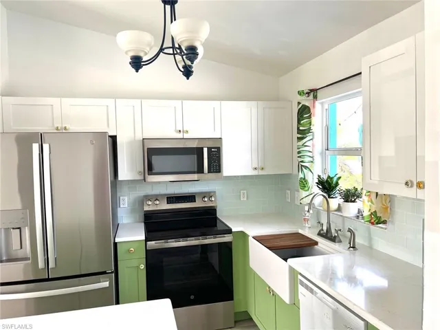 Kitchen featuring appliances with stainless steel finishes, white cabinetry, green cabinetry, and pendant lighting