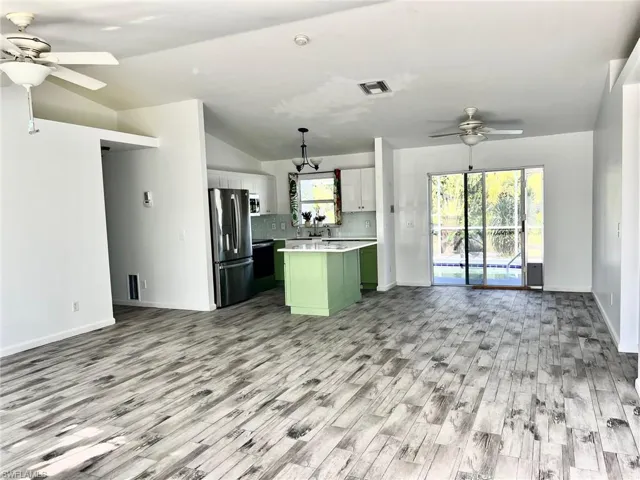 Kitchen with stainless steel appliances, decorative light fixtures, white cabinets, a kitchen island, and lofted ceiling