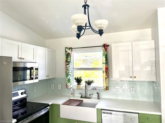 Kitchen with white cabinetry, pendant lighting, vaulted ceiling, decorative backsplash, and appliances with stainless steel finishes