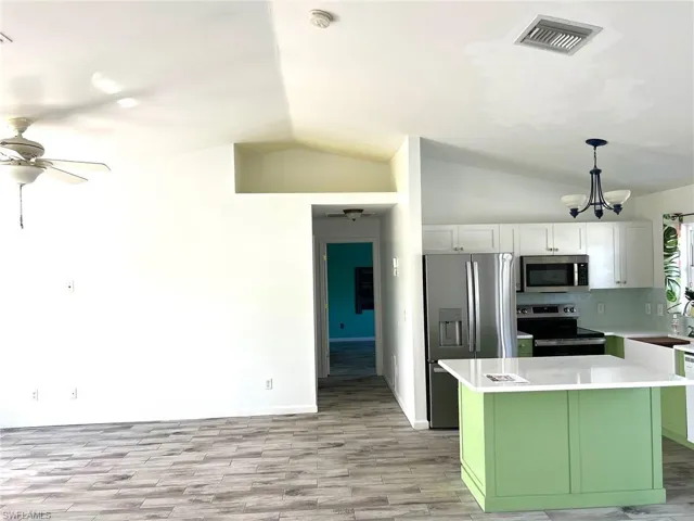 Kitchen with pendant lighting, lofted ceiling, decorative backsplash, white cabinetry, and stainless steel appliances