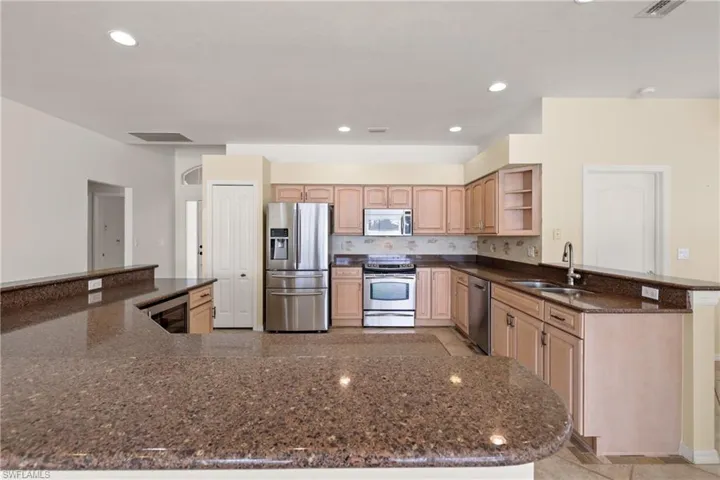 Remodeled kitchen featuring stainless steel appliances, kitchen peninsula, beverage cooler, wood cabinets and granite countertops.