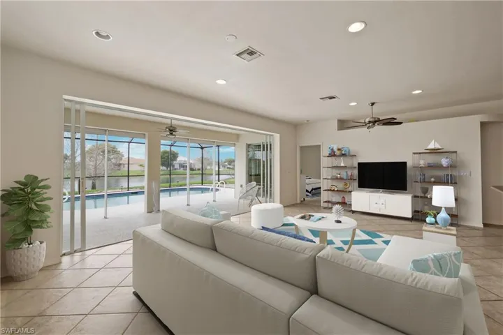 Tiled living room with ceiling fan and full wall sliding glass doors to screened lanai and pool.