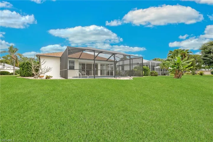 Back of house with a screened lanai and a lush lawn