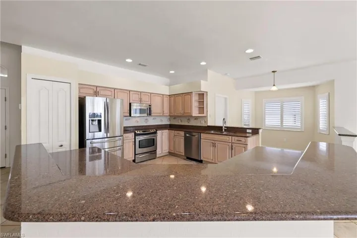 Kitchen with decorative backsplash, appliances with stainless steel finishes, wood cabinetry, lighting, and sink
