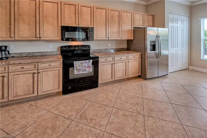 Kitchen with light tile patterned floors, black appliances, crown molding, and light stone countertops