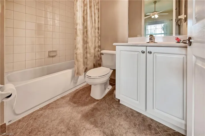 Full bathroom featuring toilet, vanity, ceiling fan, shower / bath combo with shower curtain, and tile patterned floors