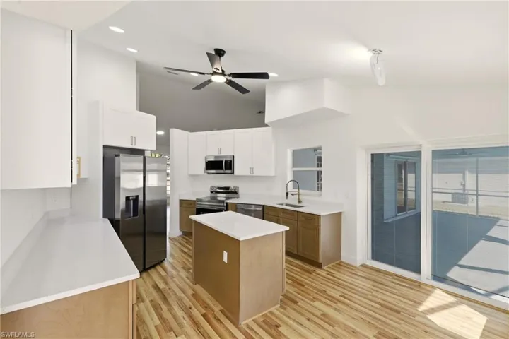 Kitchen with stainless steel appliances, light wood-type flooring, a ceiling fan, dual tone cabinets, and lofted ceiling