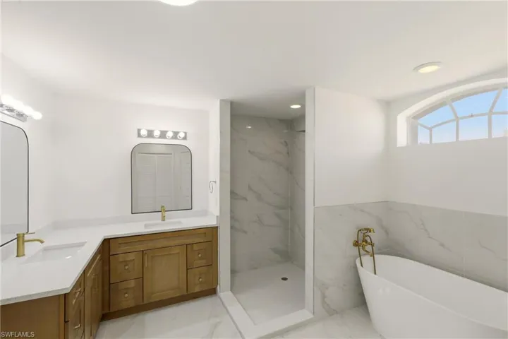 Bathroom with light marble finish flooring, a soaking tub, double vanity, a marble finish shower, and recessed lighting