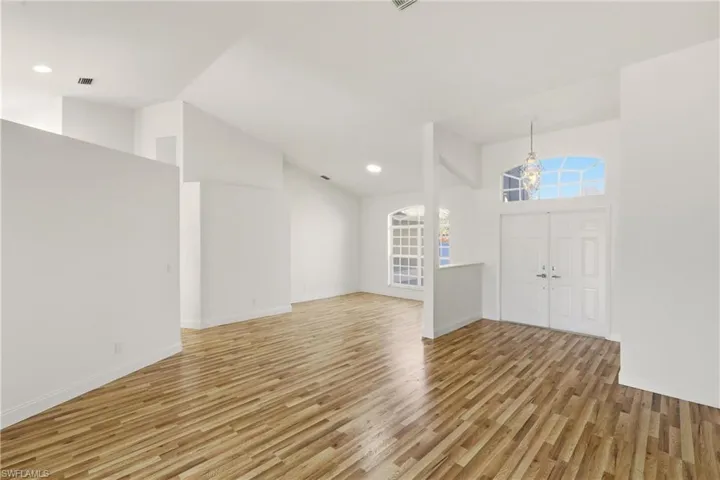 Entrance foyer with light wood-style flooring, vaulted ceiling, and a chandelier