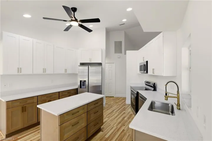 Kitchen featuring dual tone cabinets, stainless steel appliances, a center island, light wood finished floors, and ceiling fan