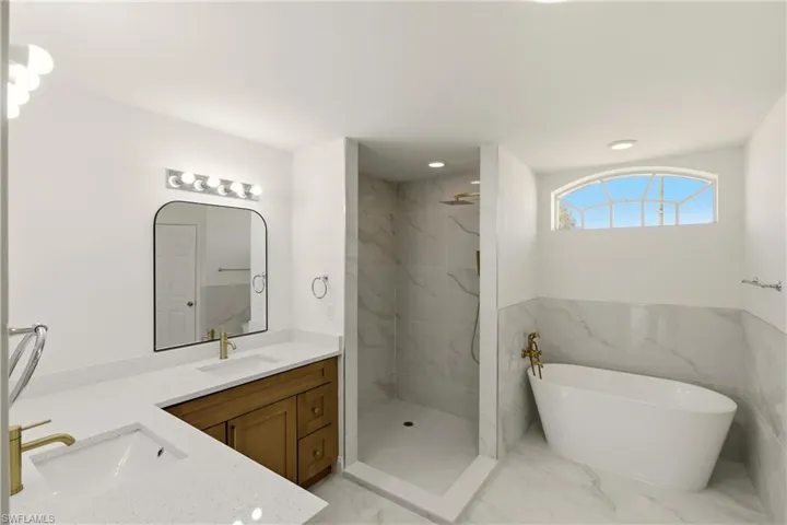 Bathroom with a marble finish shower, double vanity, a soaking tub, light marble finish floors, and recessed lighting