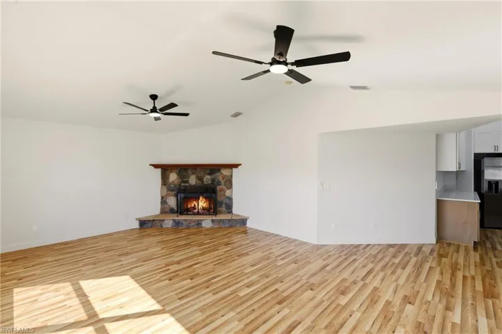 Unfurnished living room with light wood-type flooring, a fireplace, vaulted ceiling, and a ceiling fan
