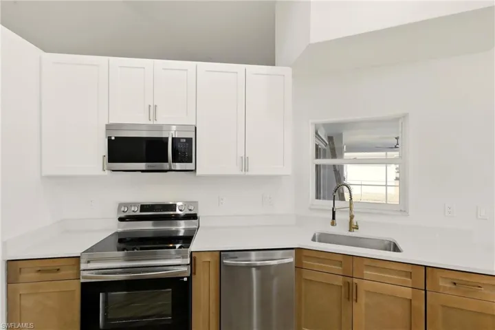 Dual tone kitchen featuring stainless steel appliances, light stone countertops, and two tone cabinets