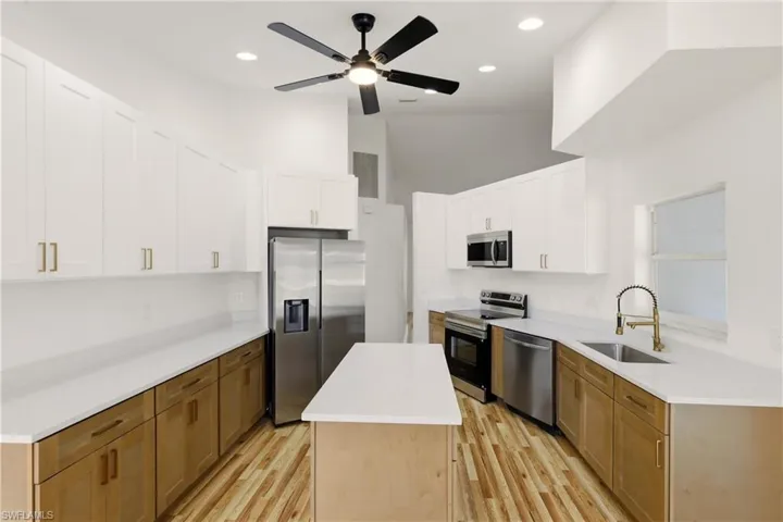 Dual tone kitchen with stainless steel appliances, a kitchen island, ceiling fan, light wood-style floors, and two tone cabinets