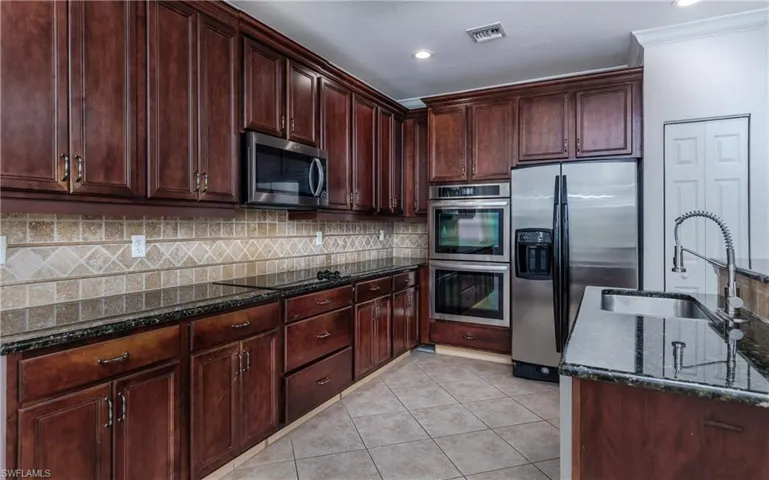 Kitchen with stainless steel appliances, light tile patterned flooring, sink, ornamental molding, and dark stone counters