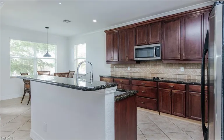 Kitchen with stainless steel appliances, dark stone countertops, an island with sink, and decorative backsplash