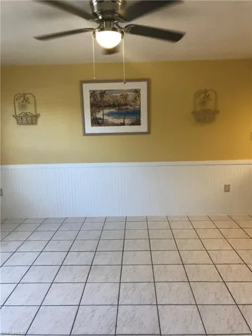 Spare room featuring a wainscoted wall, ceiling fan, and tile patterned flooring