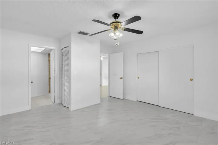 Unfurnished bedroom featuring two closets, a textured ceiling, light marble finish flooring, and ceiling fan