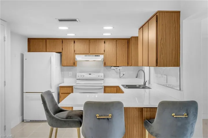 Kitchen with a breakfast bar area, white appliances, a peninsula, light stone countertops, and brown cabinetry