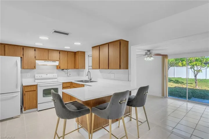 Kitchen featuring white appliances, a breakfast bar area, a peninsula, brown cabinetry, and under cabinet range hood