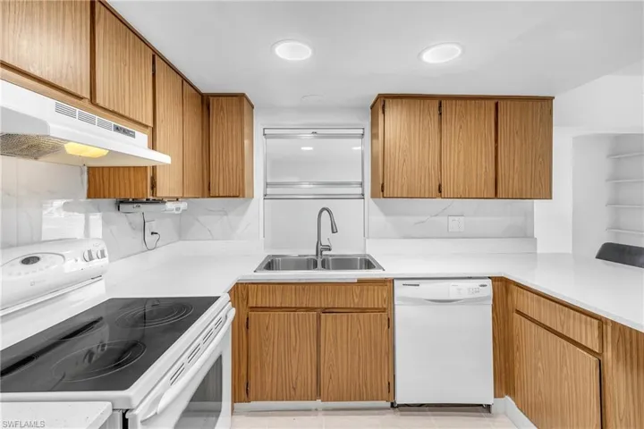 Kitchen featuring white appliances, brown cabinets, under cabinet range hood, and light stone countertops