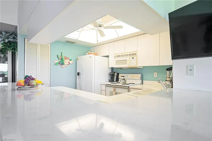 Kitchen featuring white appliances, light stone counters, white cabinetry, and a ceiling fan