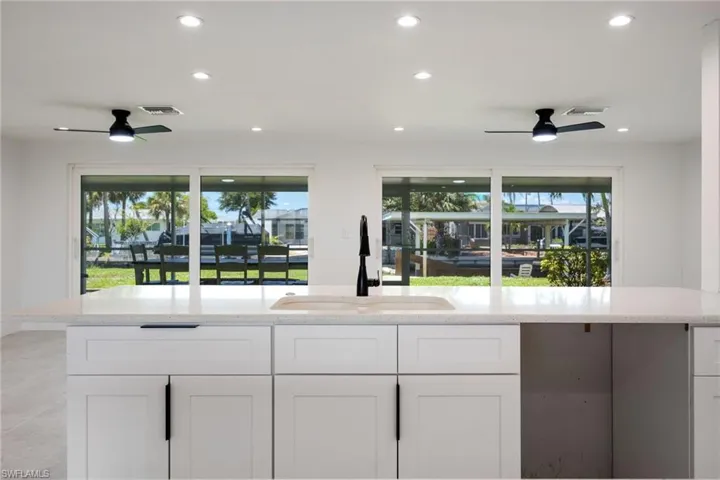 Kitchen with recessed lighting, light stone countertops, white cabinetry, and expansive windows showcasing waterfront views.