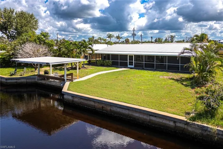 Back of property with screened lanai, metal roof, covered boathouse, concrete seawall, and plenty of yard space for a pool.