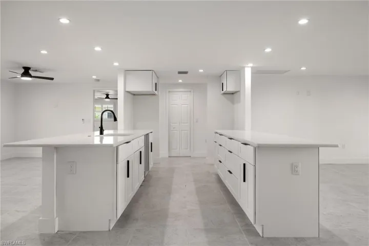 Sleek kitchen with dual peninsulas, light stone countertops, recessed lighting, breakfast bar seating, and modern white cabinetry.