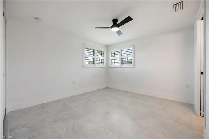 Guest bedroom with ensuite full bath, tile flooring, plantation shutters, and ceiling fan
