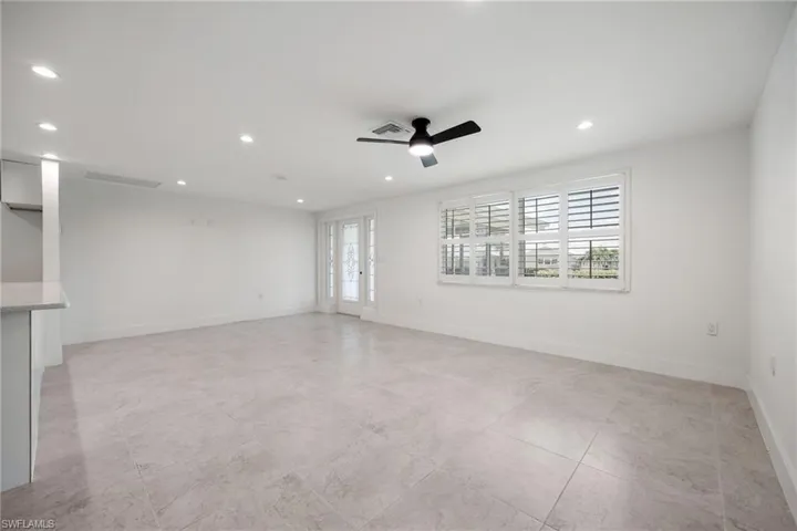 Light-filled living area with neutral tile flooring, plantation shutters, and access to the front entry