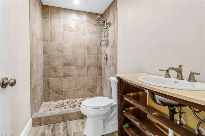 Guest house bath athroom with tiled shower, wood-type flooring, sink, and toilet