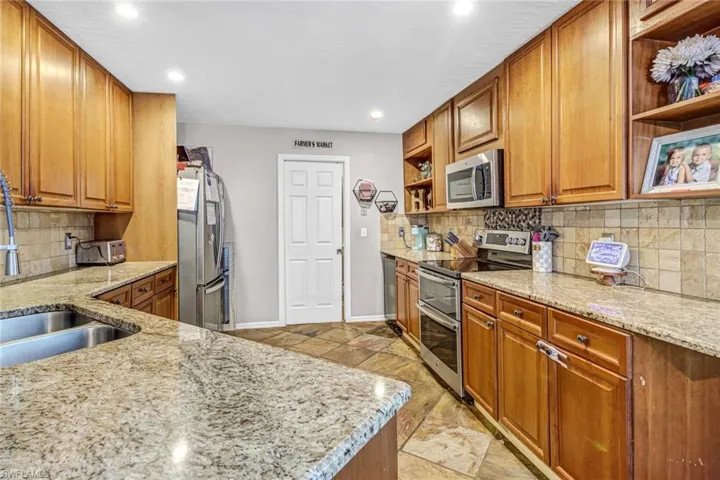 Kitchen featuring appliances with stainless steel finishes, light stone counters, backsplash, and light tile floors