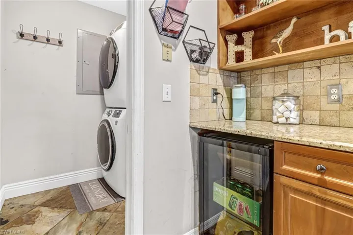 Laundry area with wine cooler, stacked washing maching and dryer, and tile floors