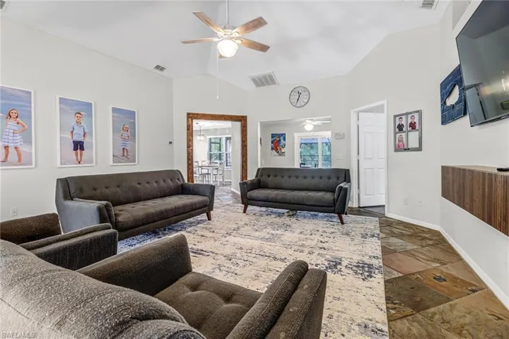 Living room featuring high vaulted ceiling, dark tile flooring, and ceiling fan