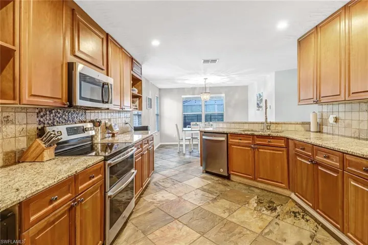 Kitchen featuring light stone countertops, appliances with stainless steel finishes, sink, tasteful backsplash, and light tile floors