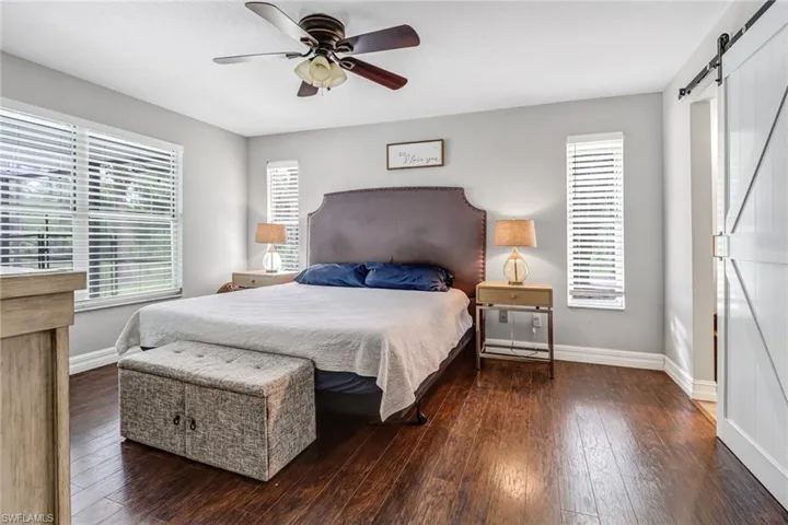 Bedroom with a barn door, ceiling fan, dark hardwood / wood-style floors, and multiple windows