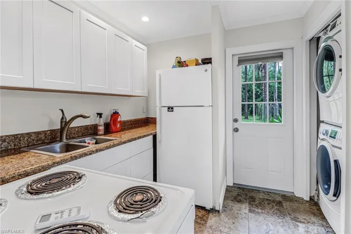 Guest house K\kitchen featuring stacked washer / drying machine, white fridge, white cabinetry, sink, and light tile floors