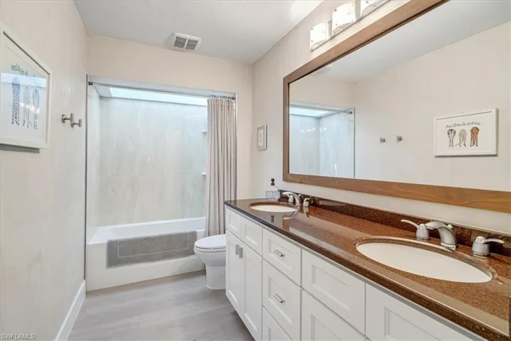 Bathroom featuring double vanity, shower / tub combo with curtain, and light wood finished floors