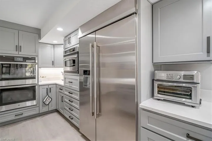 Kitchen featuring gray cabinetry, appliances with stainless steel finishes, recessed lighting, light wood-style flooring, and light stone counters