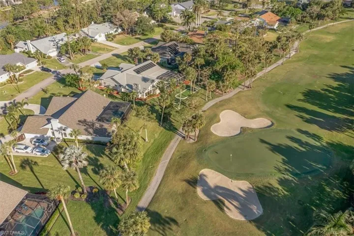 Aerial view of property and surrounding area featuring a golf course and nearby suburban area